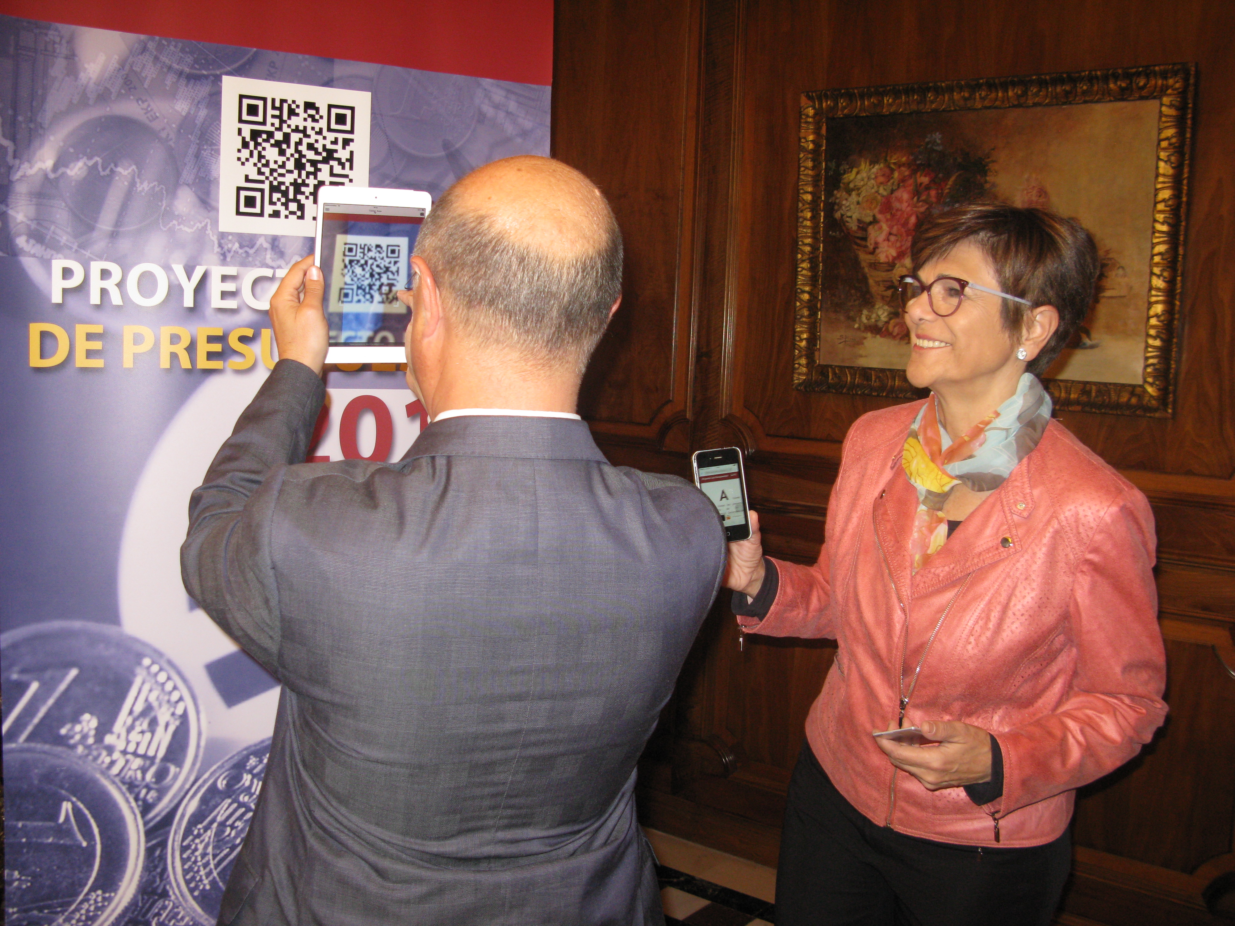 El consejero de Hacienda, Andrés Carrillo, muestra a la presidenta de la Asamblea, Rosa Peñalver, cómo consultar el proyecto de ley de Presupuestos a través del código QR.