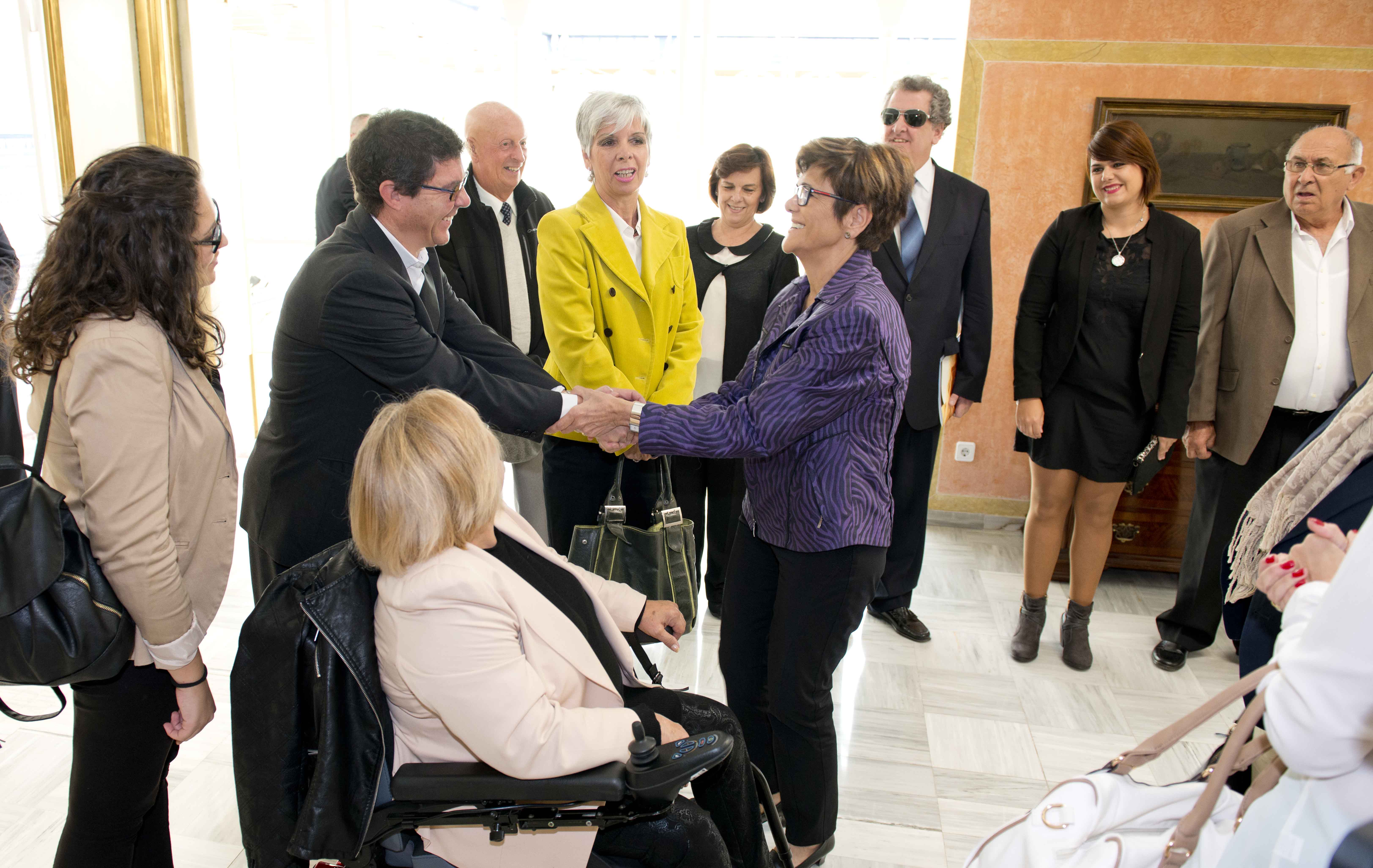 La presidenta de la Asamblea, Rosa Peñalver, saluda a Lola Valverde, de la Comisión de Accesibilidad de ASPAYM